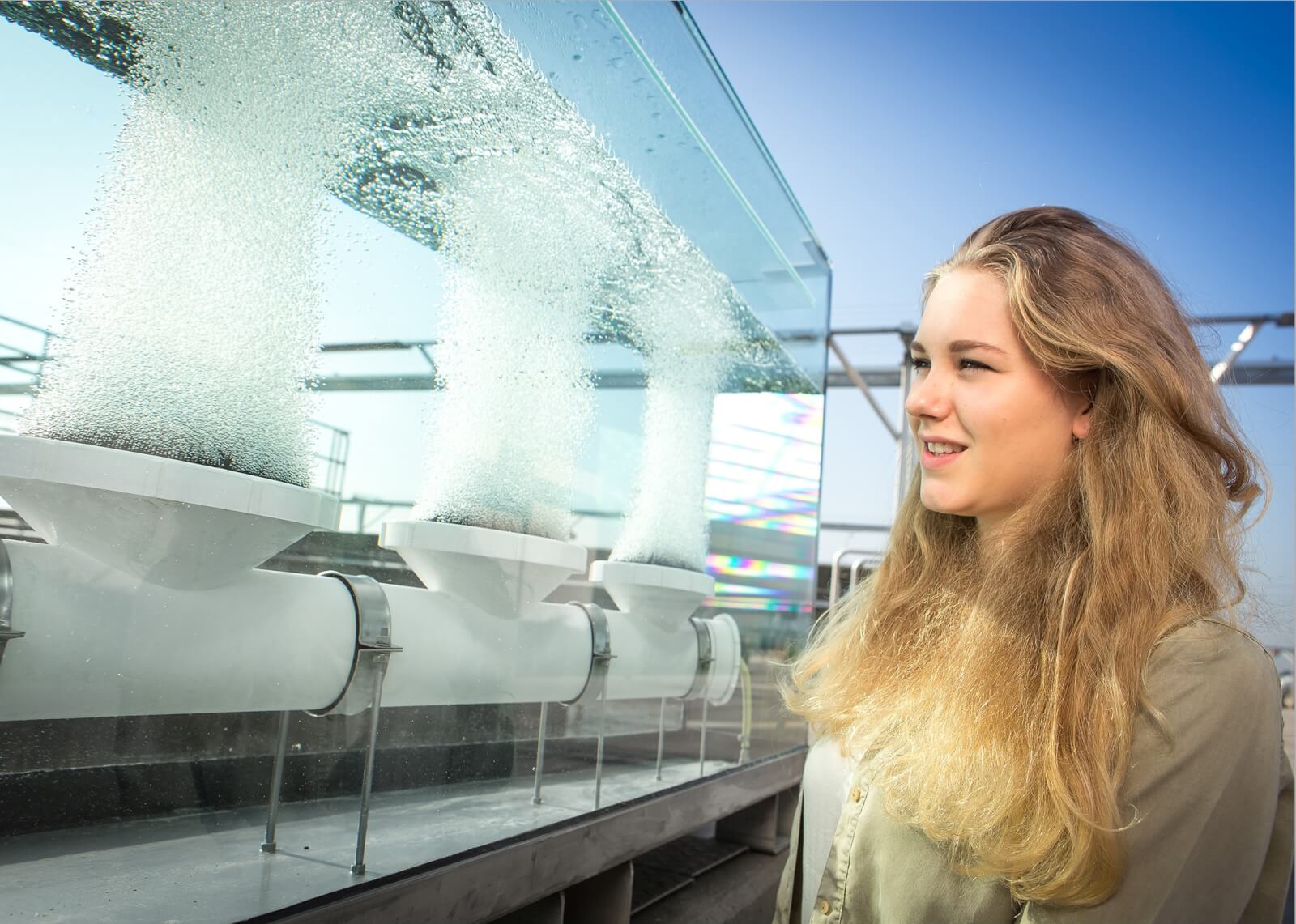 Besucherin vor einem Glaskasten, in dem drei Tellerbelüfter Luftblasen ausstoßen. © Christian Houdek